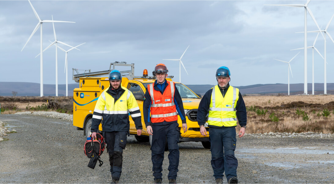 Technicians walking with wind turbine and a van in the background