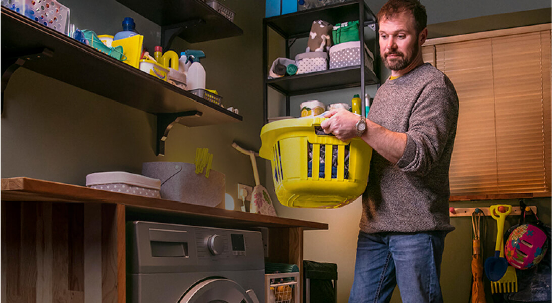 Man standing in front of his washing machine with a basket full of clothes