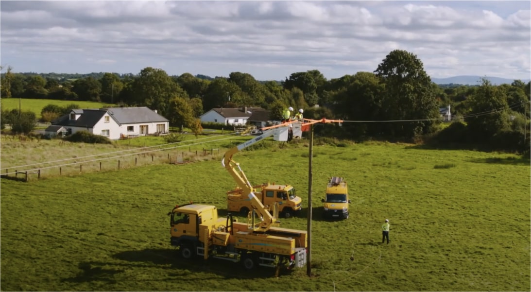 Technicians in a field performing work using a cherry picker to fix electricity poles