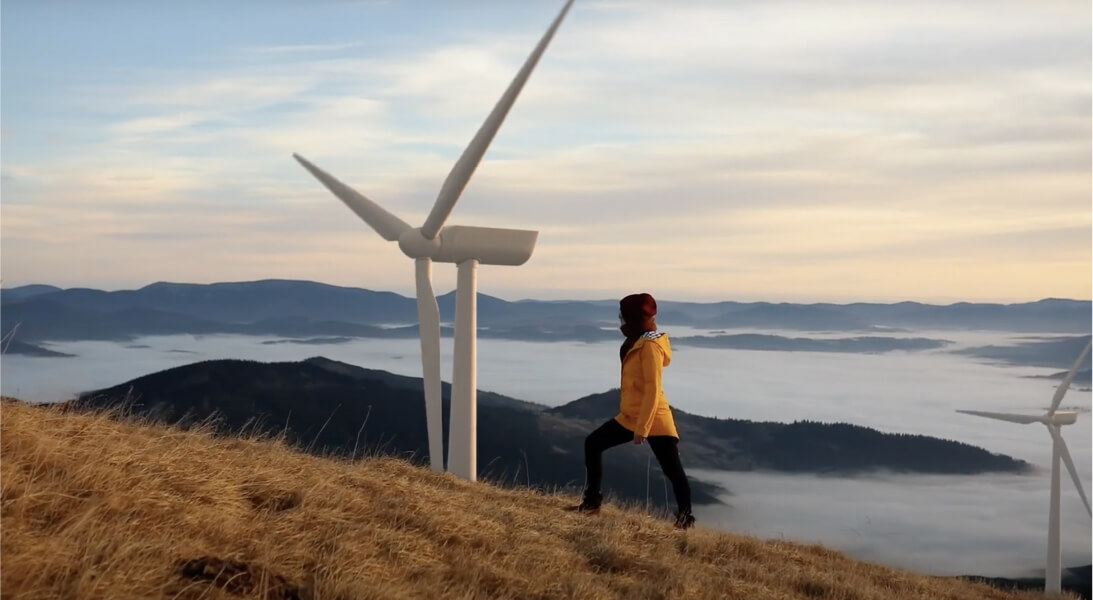 Woman climbing hill with wind turbine and island in the background