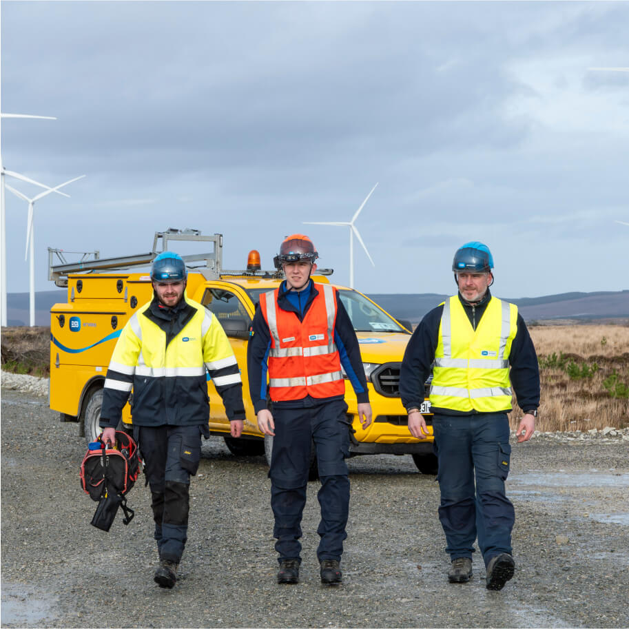 Technicians walking with a van and wind turbine behind them