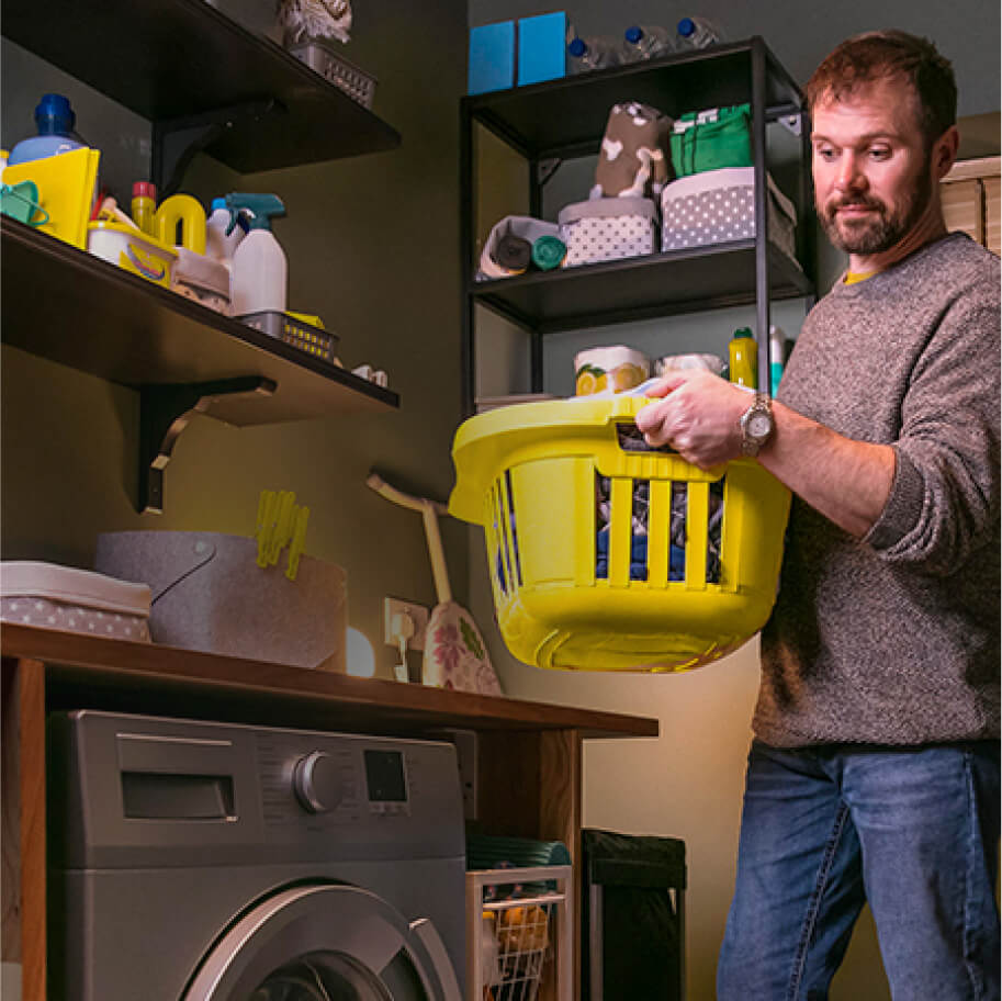 Man looking at his washing machine with a basket of clothes to wash