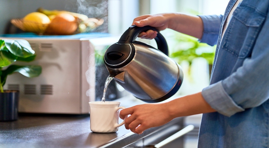 A woman pouring hot water from a kettle into a cup.