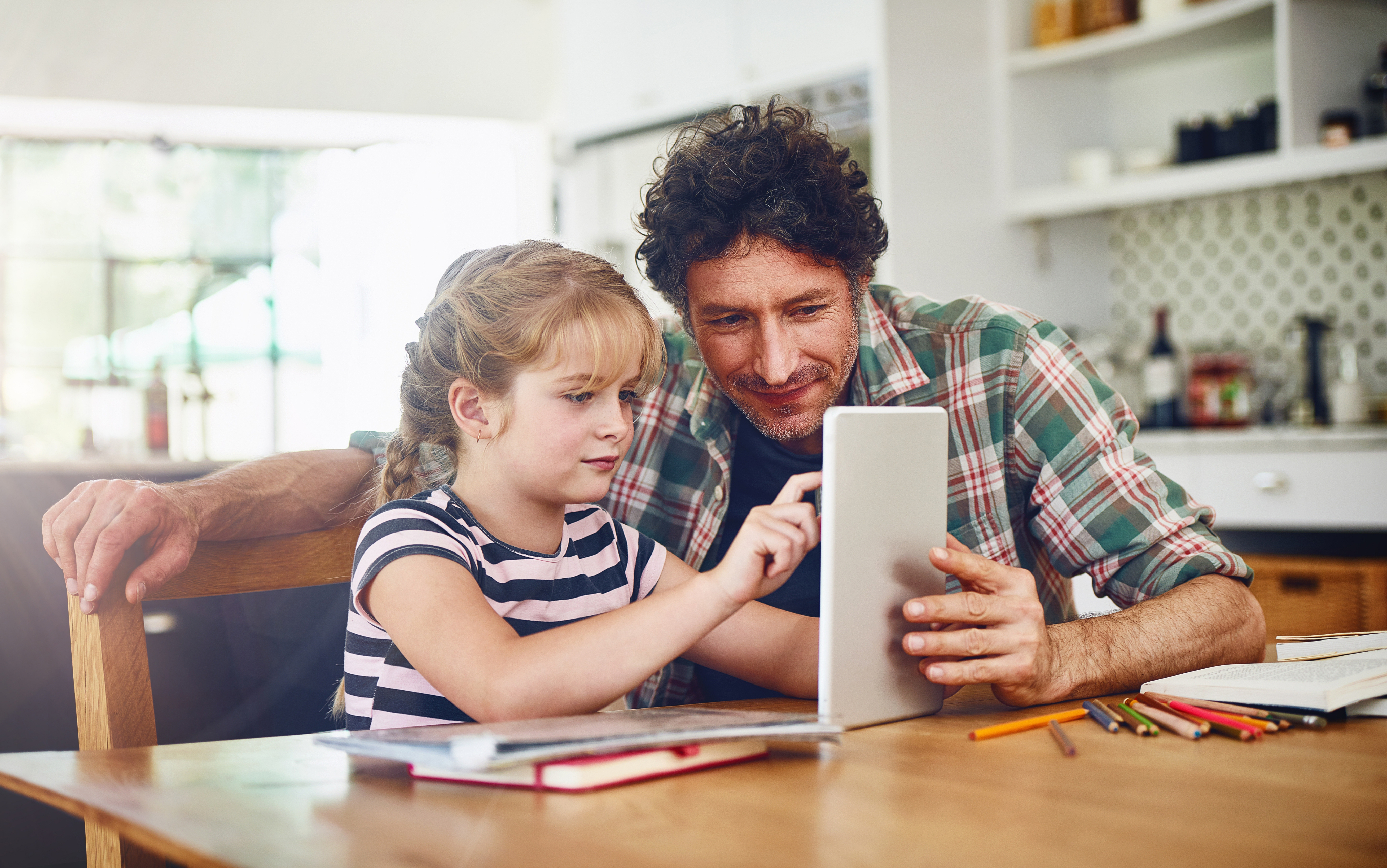 A man and girl sitting at a table using a tablet.