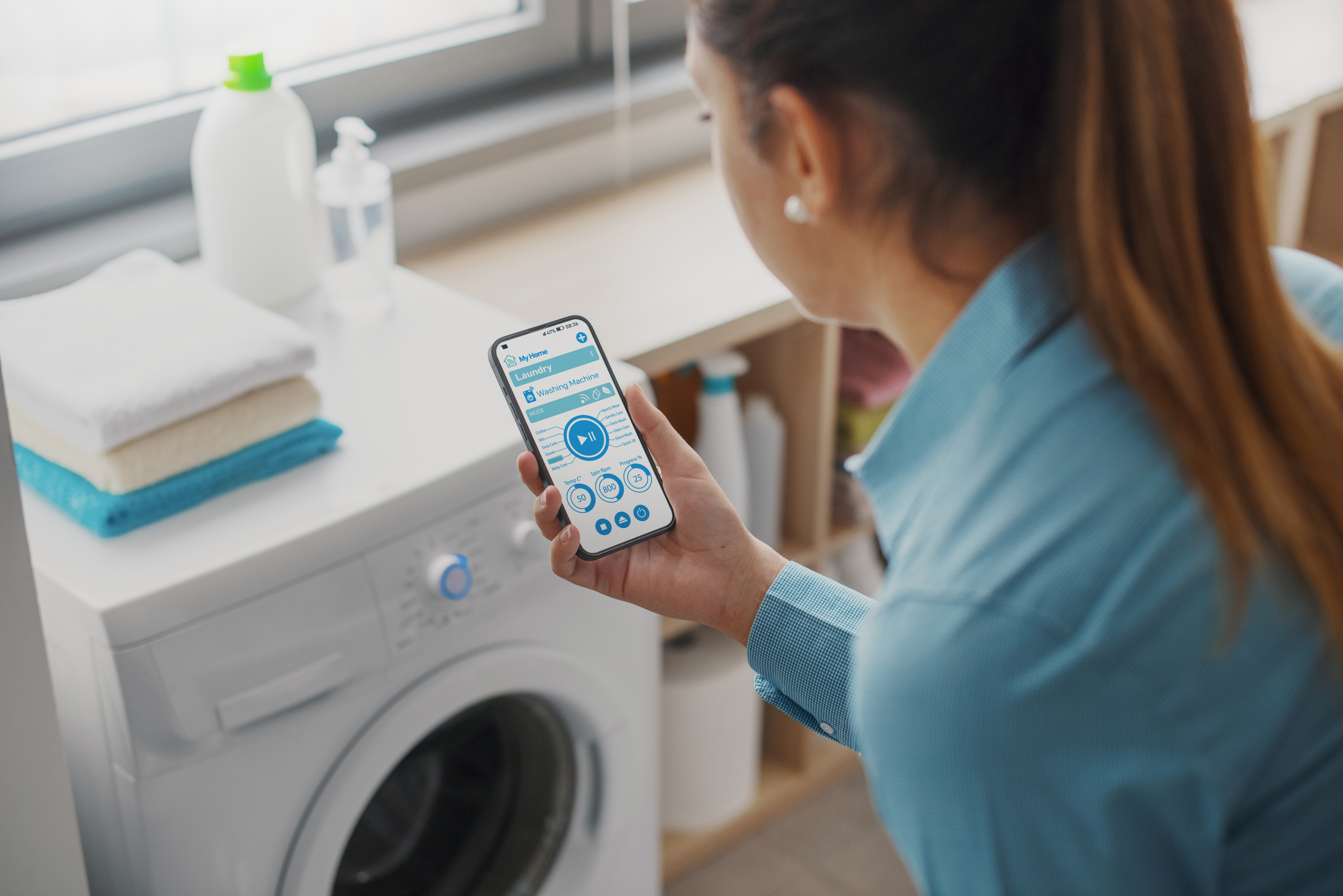 A woman using her phone near a washing machine.