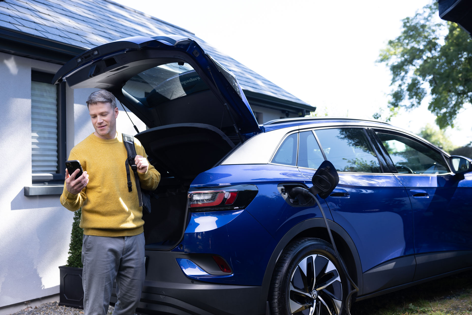 A man is charging his blue electric car and holding a phone.